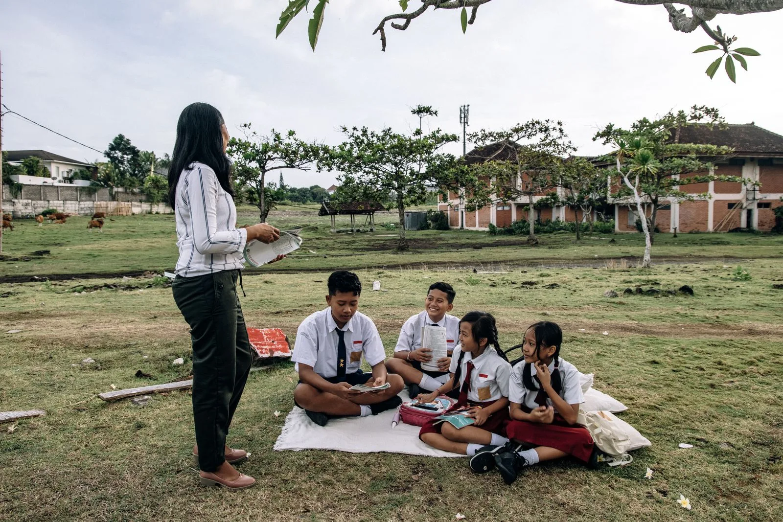 A teacher reading with a group of students outdoors at school