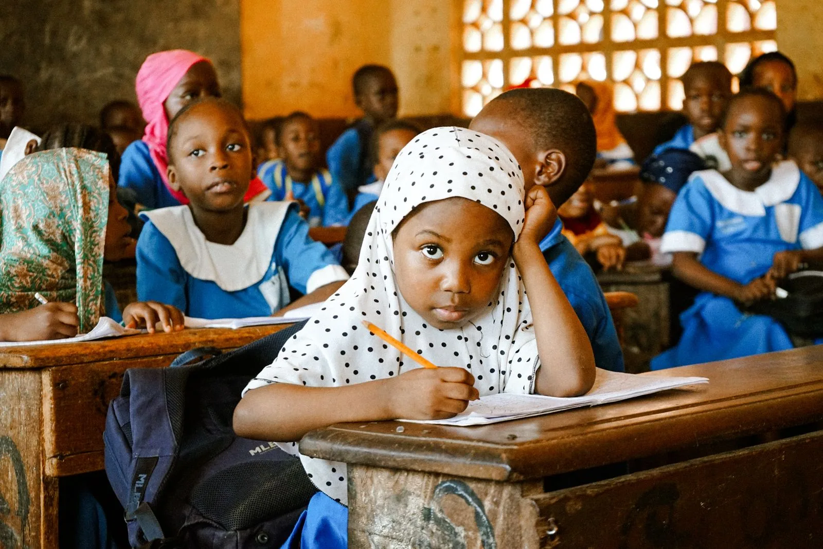 Young students writing in their notebooks during a lesson in a busy primary school classroom