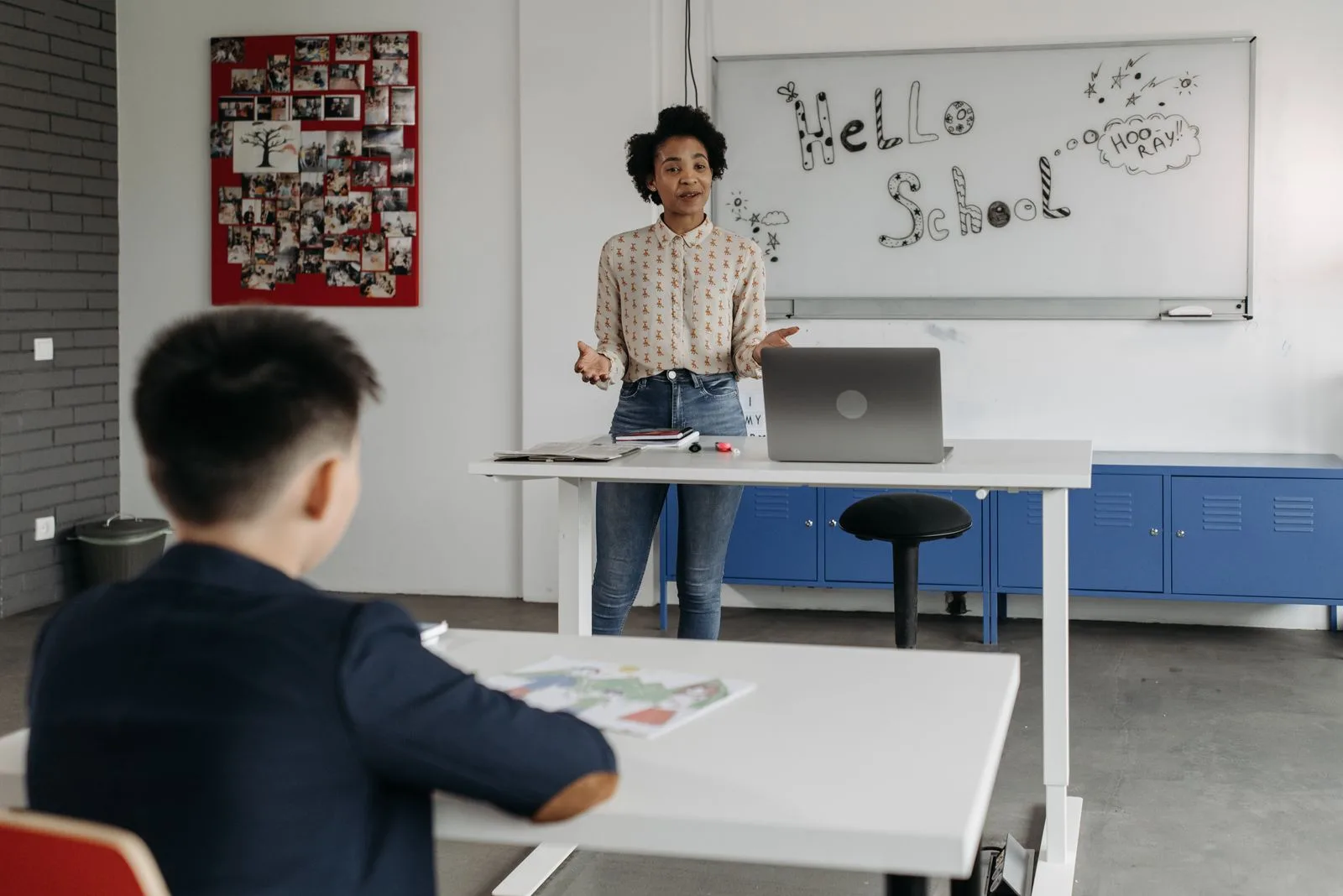 A teacher standing at her laptop, addressing students in a bright, modern classroom